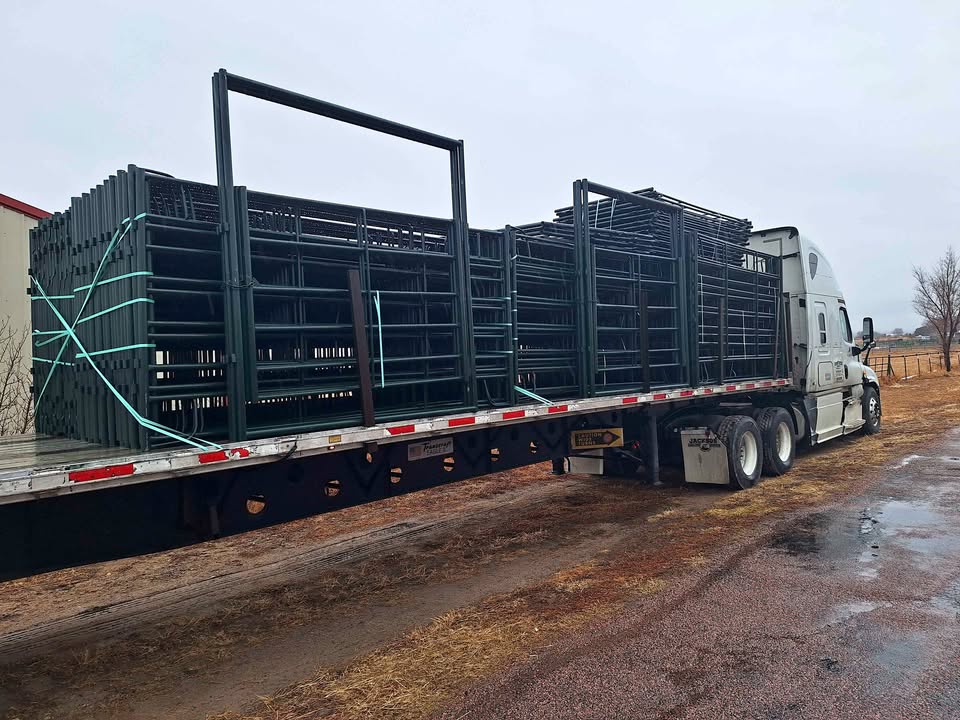 Flatbed truck loaded with green powder-coated round-tube livestock panels